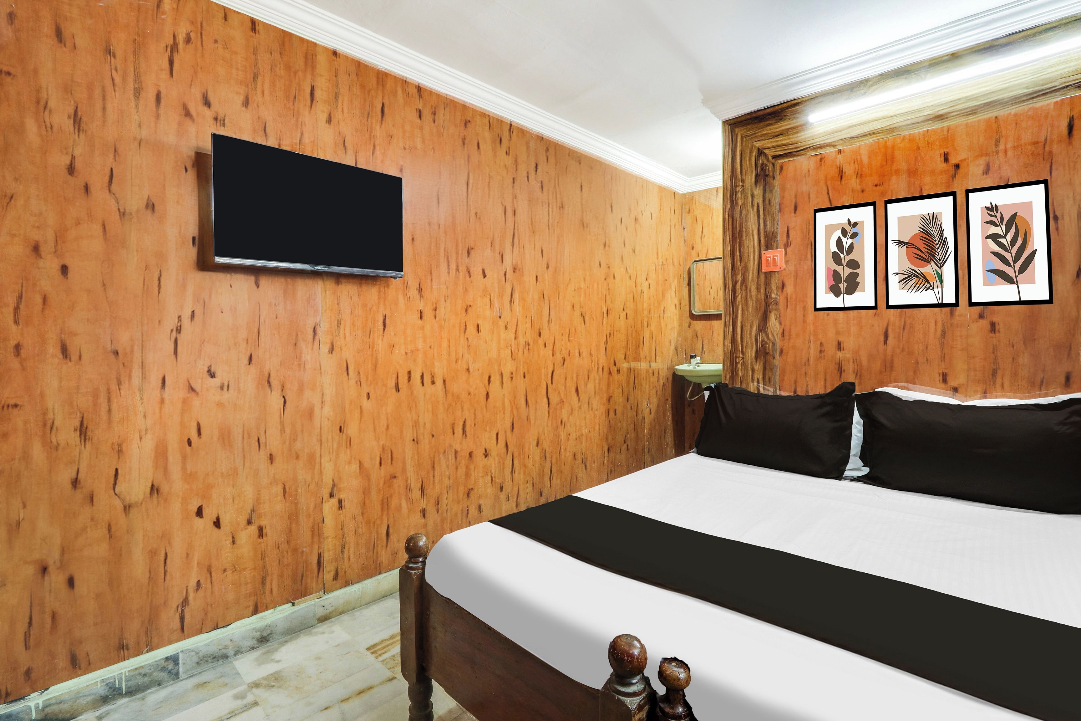 Ein Hotelzimmer mit einem großen Bett, Holzwänden, einem flachbildfernseher an der Wand und drei gerahmten Kunstwerken an der Wand.