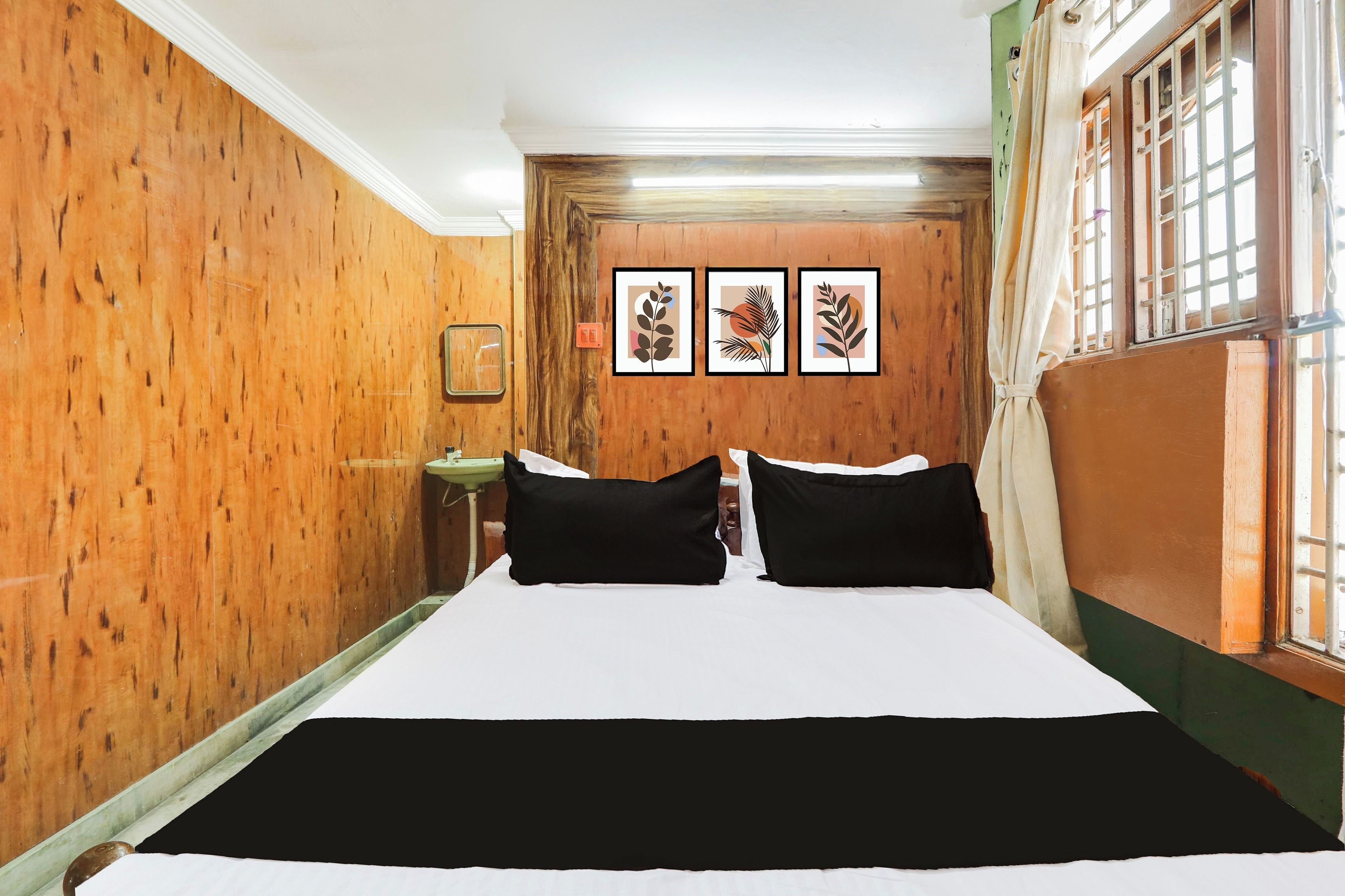 Ein Hotelzimmer mit einer Holzwand, einem Bett mit schwarz-weißer Bettwäsche und drei gerahmten Pflanzenbildern an der Wand.