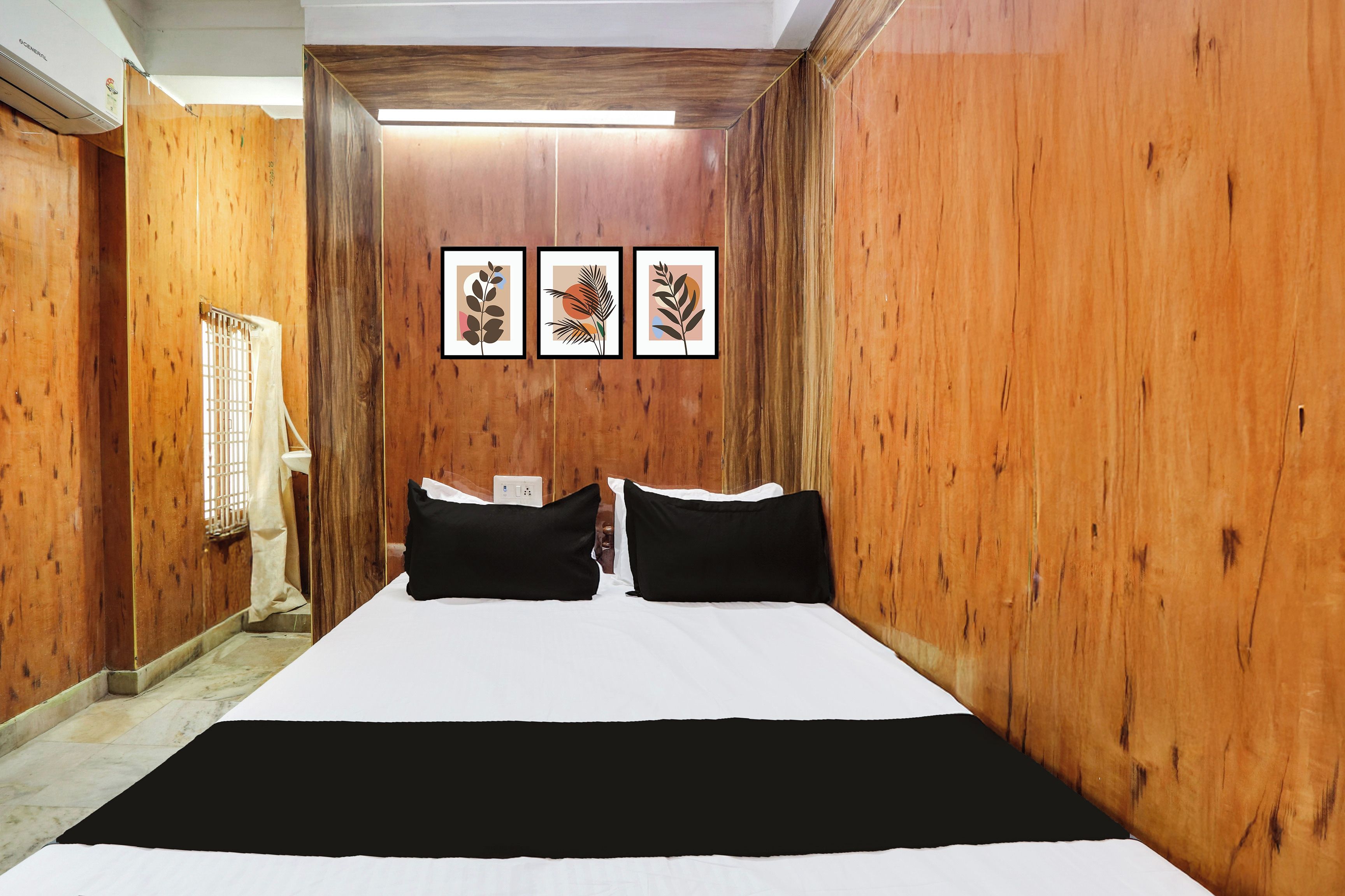 Habitación de hotel con pared de madera, cama con ropa de cama blanco y negro, y tres cuadros en la pared.