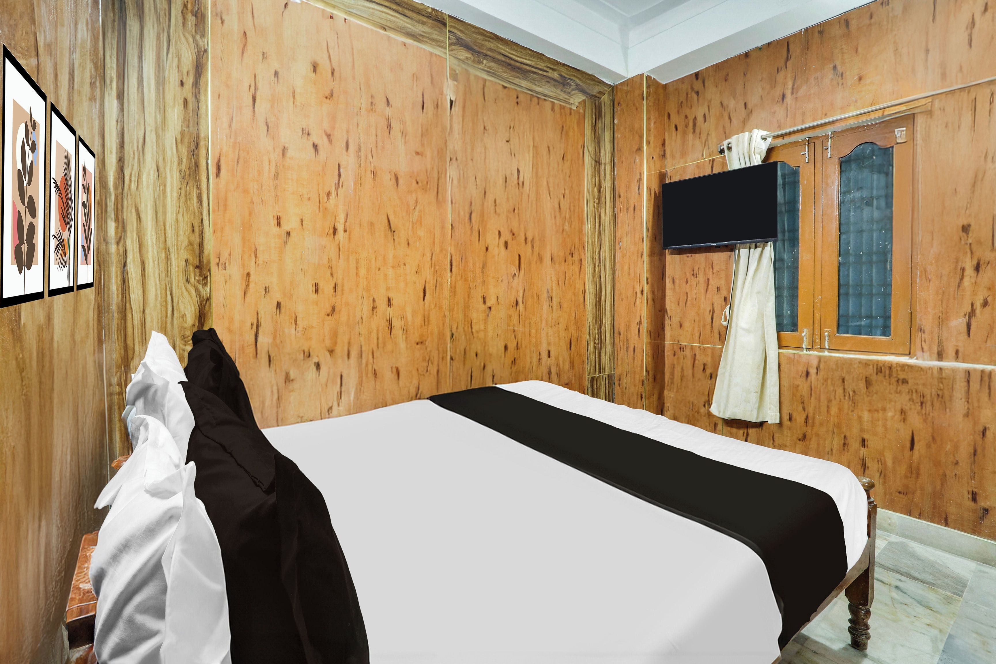 Quarto de hotel com parede de madeira, cama com roupa de cama preta e branca, janela com cortinas e um quadro na parede.