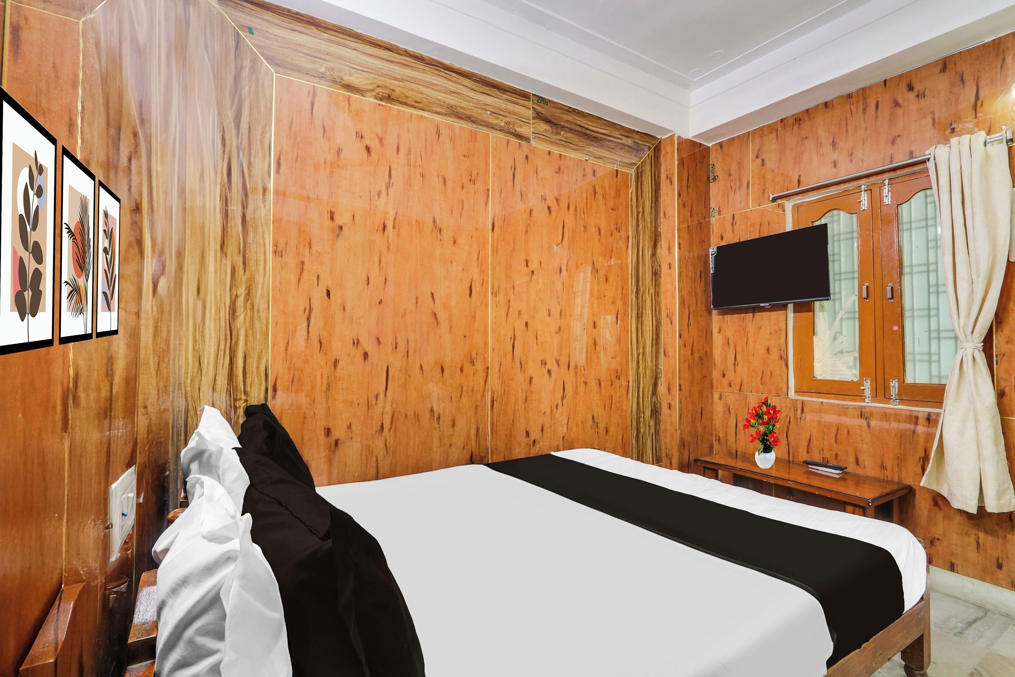 Een hotelkamer met een wand van houten lambrisering, een bed met zwart-wit beddengoed, een flatscreen televisie aan de wand bevestigd, een houten bureau met een bloevas, en een raam met gordijnen.