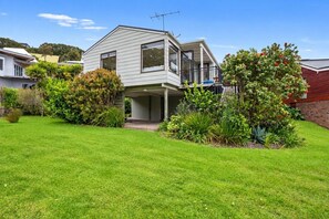 A two-story house with a covered porch, surrounded by a well-maintained lawn and various plants. - Sandy Feet Beach House - right across from Onemana Beach (Onemana)