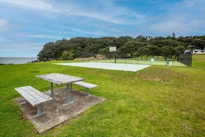 An outdoor basketball court with a picnic table, surrounded by grass and trees, under a clear sky. - Sandy Feet Beach House - right across from Onemana Beach (Onemana)
