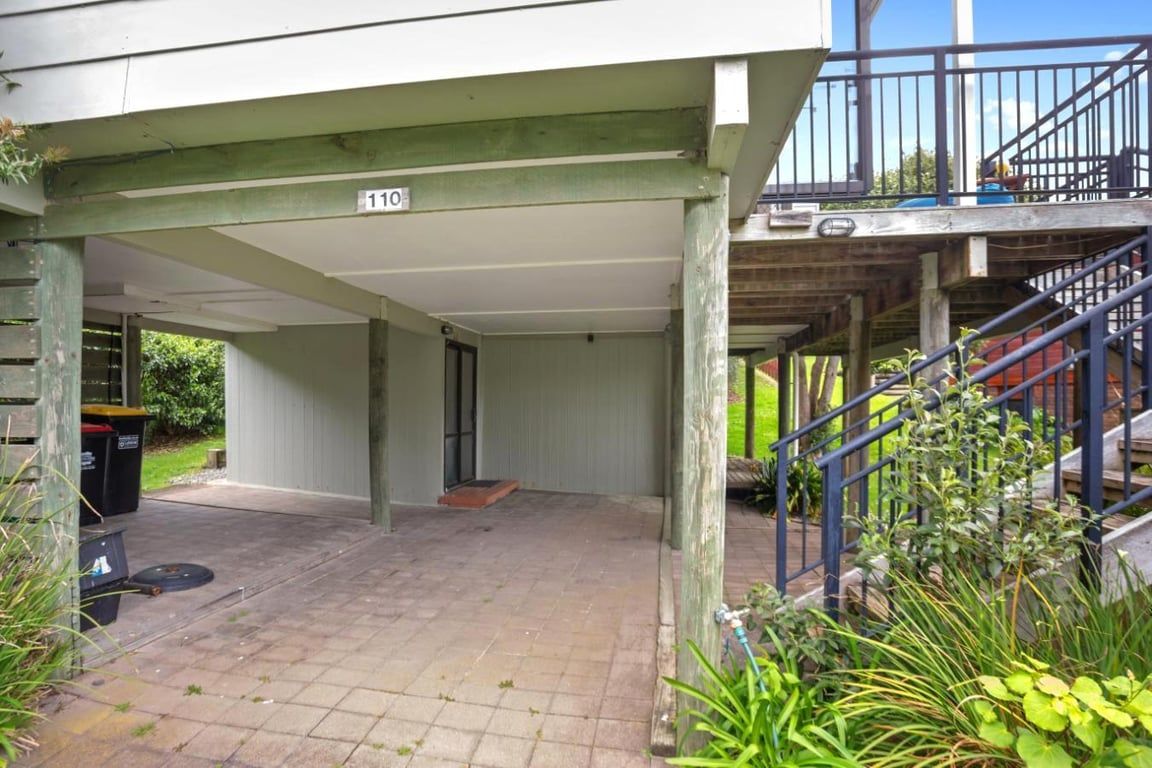 A covered outdoor area with a staircase leading to an upper level, a trash bin, and a number sign indicating the location.