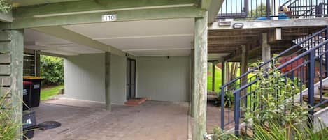 A covered outdoor area with a staircase leading to an upper level, a trash bin, and a number sign indicating the location.