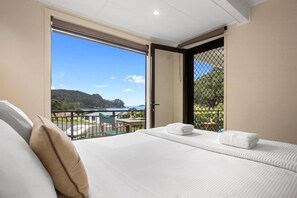Una camera d'hotel con un letto grande, un balcone vista mare e una zona pranzo visibile attraverso la porta aperta.