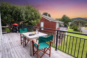 Un terrazzo in legno con tavolo e sedie, un barbecue e vista su una casa e il paesaggio circostante.
