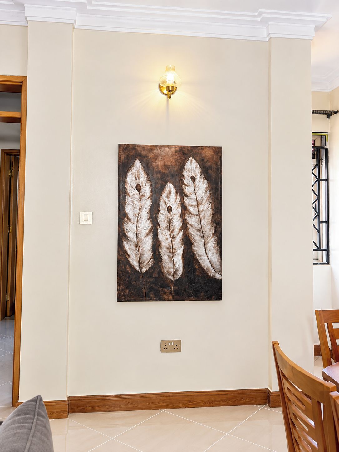 Un comedor con una obra de arte colgada en la pared con diseños similares a plumas, una lámpara sobre la mesa y una puerta que da a otra habitación.