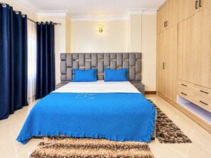 A bedroom with a bed, a headboard, a wardrobe, and a rug. - Serene Harmony Homes (Kampala)