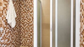 A bathroom with a checkered tile wall, a white towel rack, a shower with a glass door, and a yellow cleaning tool on the floor.