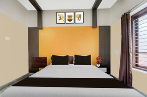 Habitación de hotel con una cama, una mesita de noche, un florero con flores y tres cuadros en la pared.