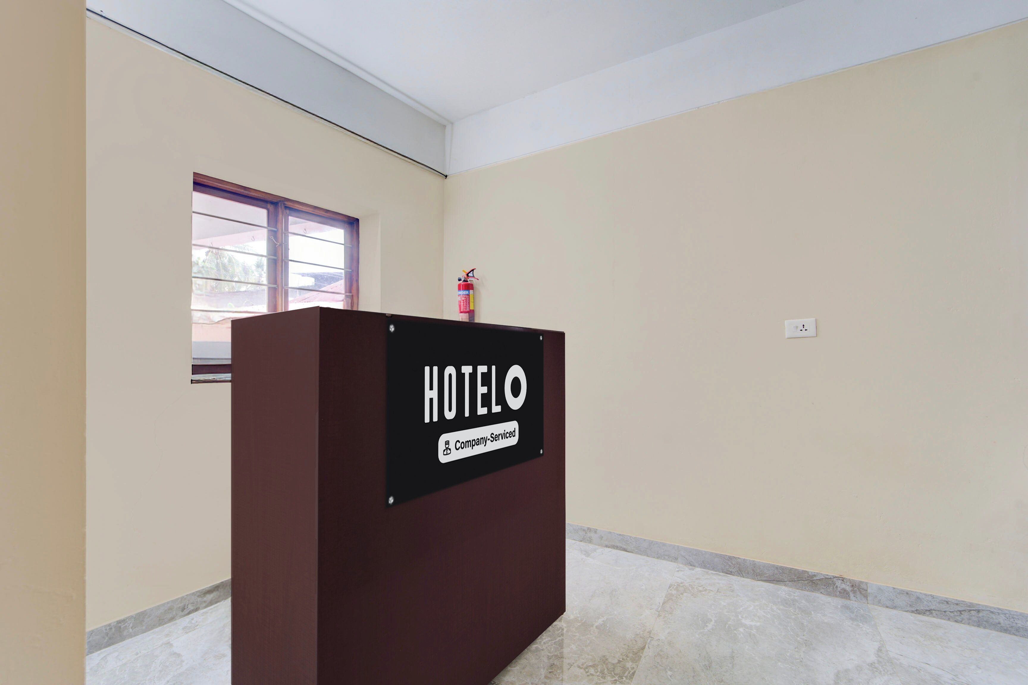 Zona de recepción de un hotel con un mostrador marrón, un extintor y una ventana con vistas al exterior.