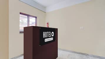 Zona de recepción de un hotel con un mostrador marrón, un extintor y una ventana con vistas al exterior.