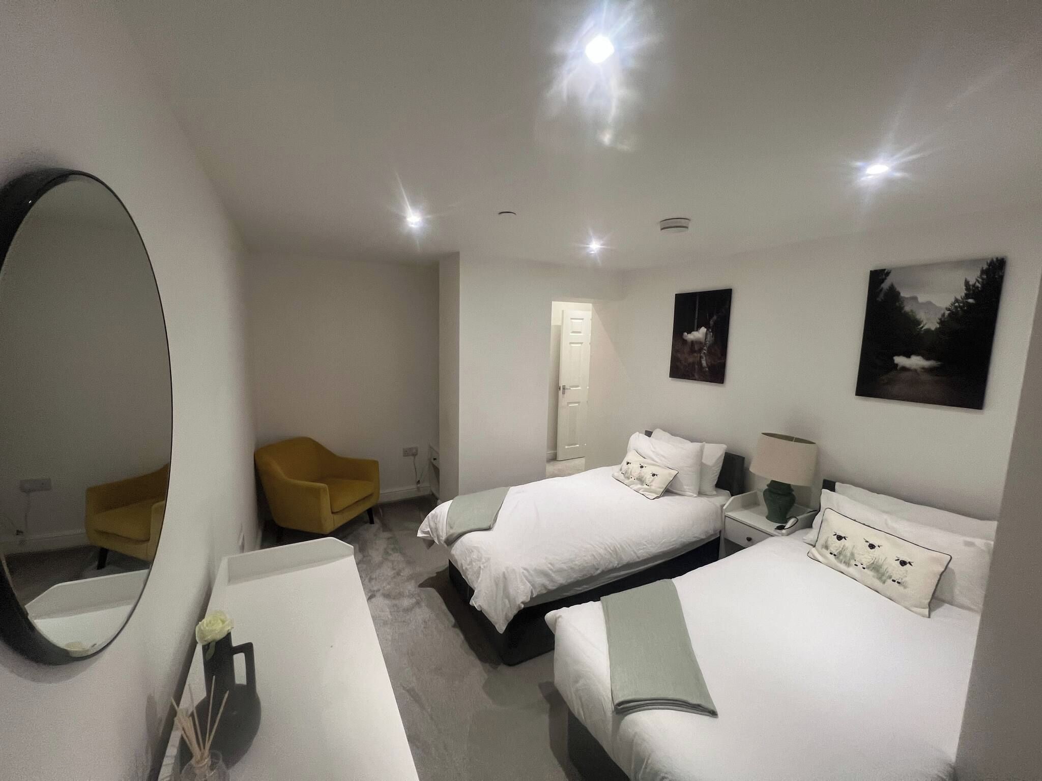 A hotel room with two beds, a large mirror, a chair, and artwork on the walls.