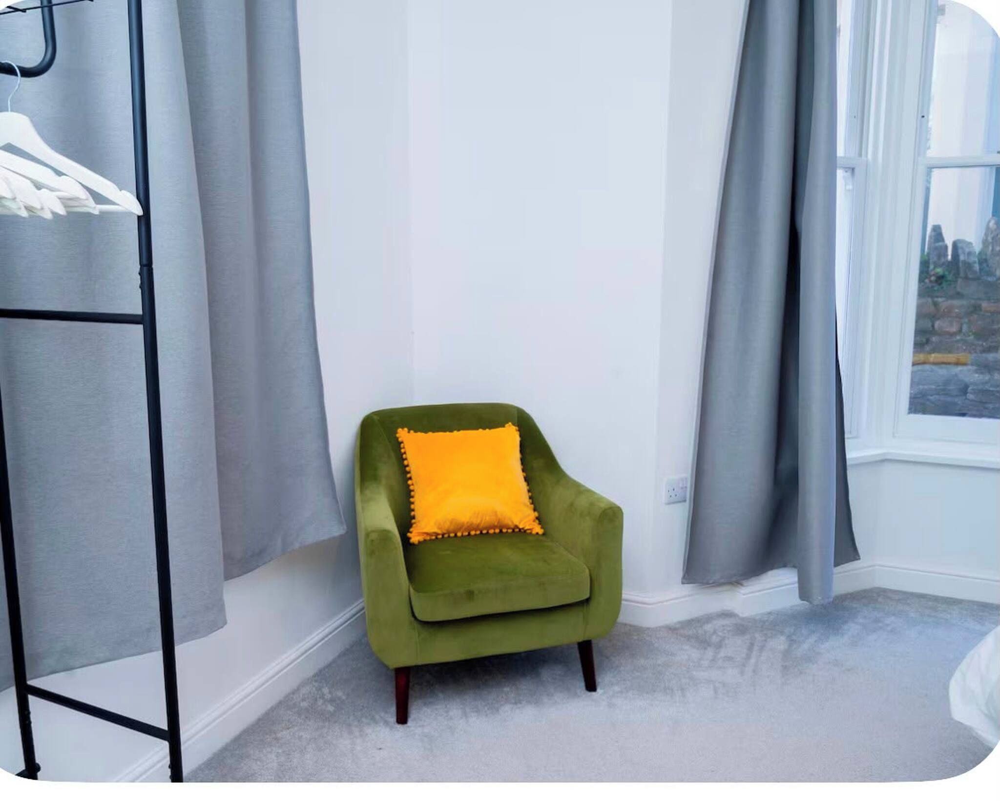 A corner room with a green armchair, a grey curtain, and a window with a view.
