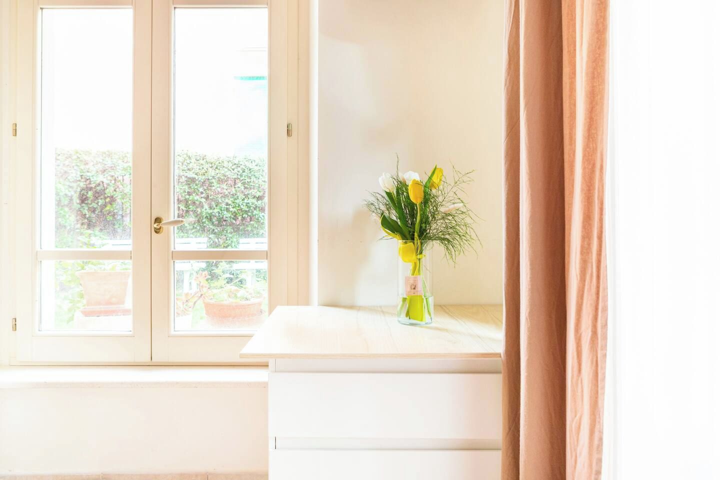 A room with a window, a vase with flowers, and a curtain.