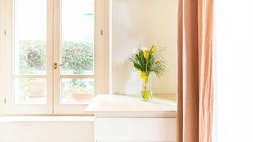 A room with a window, a vase with flowers, and a curtain.