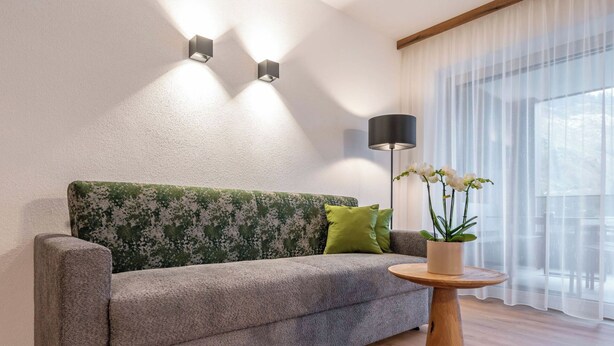 Ein modernes Wohnzimmer mit einem grauen Sofa, grün gemusterten Kissen, einem runden Couchtisch aus Holz und einer Topf-Orchidee.