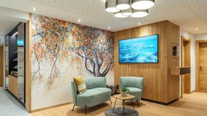 Eine moderne Lobby mit einer großen, abstrakten Wandmalerei, einem hölzernen Empfangsbereich und einer Sitzecke mit einem runden Tisch.