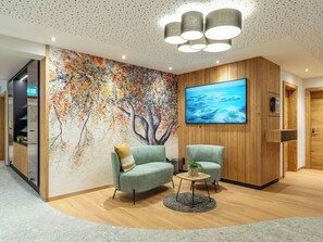 Un vestíbulo moderno con un gran mural abstracto, un mostrador de recepción de madera y una zona de estar con una mesa redonda.