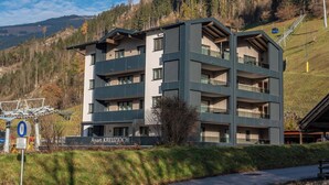 Ein mehrstöckiges Gebäude mit Balkonen, mit der Beschriftung 'Apart KREUZJOCH', vor einer Bergkulisse.