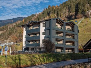 Un edificio de varios pisos con balcones, identificado como 'Apart KREUZJOCH', con montañas al fondo.