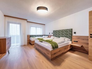 Una habitación de hotel moderna con dos camas de madera, un tocador de madera, un escritorio y un gran ventanal con cortinas translúcidas.