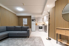 A modern living room with a grey sofa, a kitchen area with white appliances, and a wooden accent wall. - Leviraitti 5 911 by Holiday in Lapland (Levi)