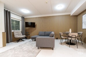 Ett modernt vardagsrum med en soffa, fåtöljer, en platt-TV, ett matbord med stolar och en vägg med ett mönster.