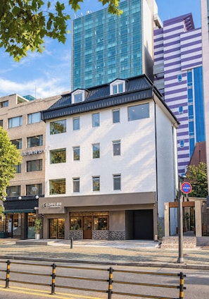 A multi-story building with a modern design, featuring a mix of glass and brick facades, and a ground-level commercial space with a visible storefront. - Grida Hongdae (Seoul)