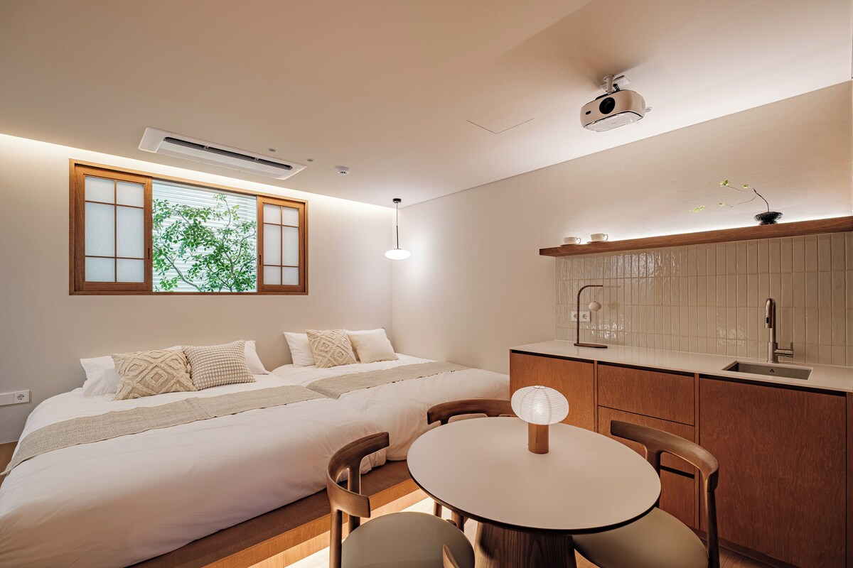 A bedroom with a bed, bedside table, and a window with a view of greenery.