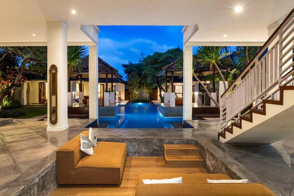 Un área de piscina lujosa con diseño moderno, una escalera y una zona de estar con cojines.