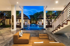 Un área de piscina lujosa con diseño moderno, una escalera y una zona de estar con cojines.