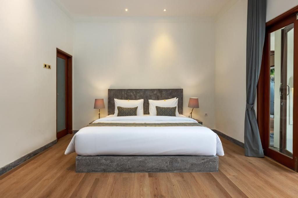 A hotel room with a large bed, two bedside lamps, and a view through a glass door.