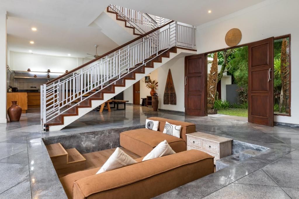 Amplia sala de estar con una escalera moderna, un conjunto de sofás y un comedor.