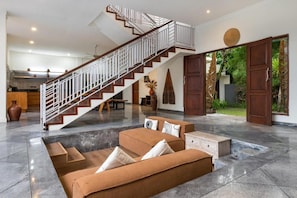 Amplia sala de estar con una escalera moderna, un conjunto de sofás y un comedor.