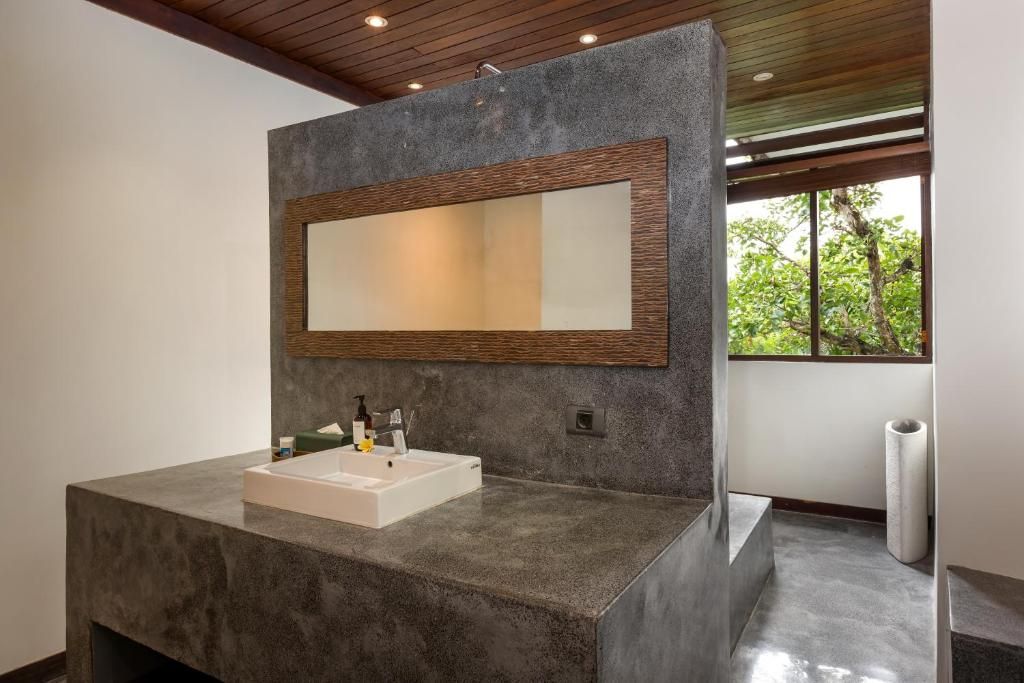 A modern bathroom with a large mirror, a rectangular sink, and a window providing natural light.