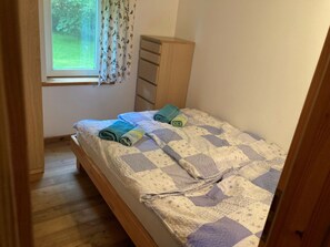 Una habitación pequeña con una cama individual, suelo de madera, ventana con vista a zonas verdes y cómoda de madera.