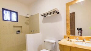 Et badeværelse med toilet, vask og brusebad. Der er et vindue over toilettet og en bøjlestang på væggen.