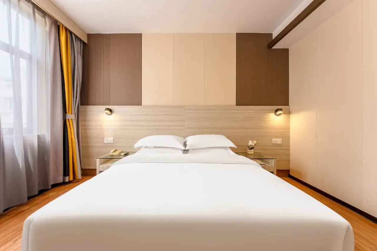Una habitación de hotel con una cama grande, mesitas de noche y una ventana con cortinas.