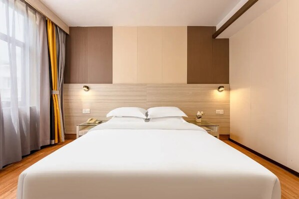 A hotel room with a large bed, bedside tables, a nightstand, and a window with curtains.