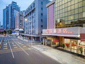 A hotel with a modern facade, a parking lot, and a street with directional arrows.