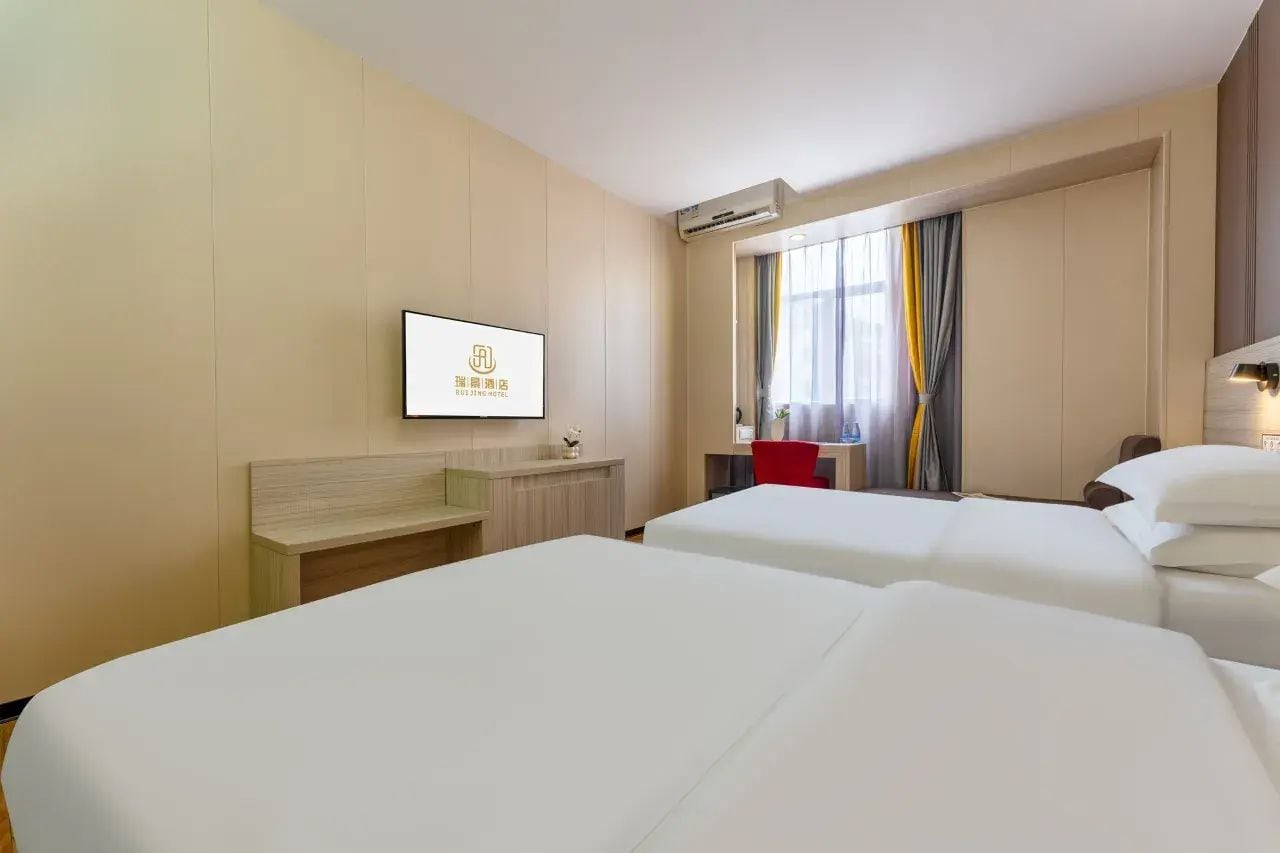 Habitación de hotel con dos camas, un escritorio, un televisor y una ventana con cortinas.