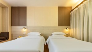 A hotel room with two beds, a sofa, and a wall-mounted light fixture. - Ruijing Hotel (Dongguan)