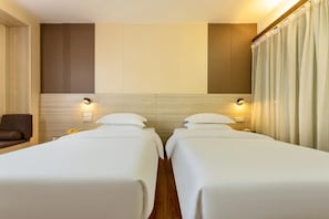 A hotel room with two beds, a sofa, and a wall-mounted light fixture. - Ruijing Hotel (Dongguan)