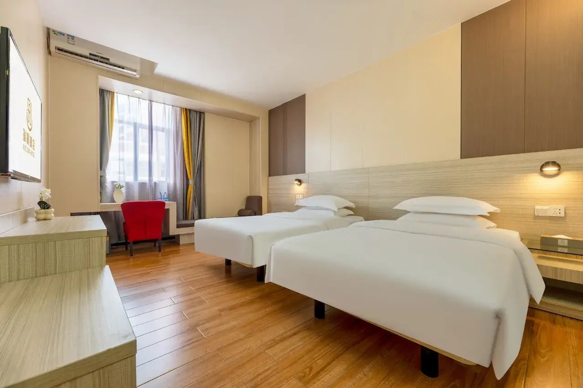 A hotel room with two beds, a desk, a chair, and a window with curtains.