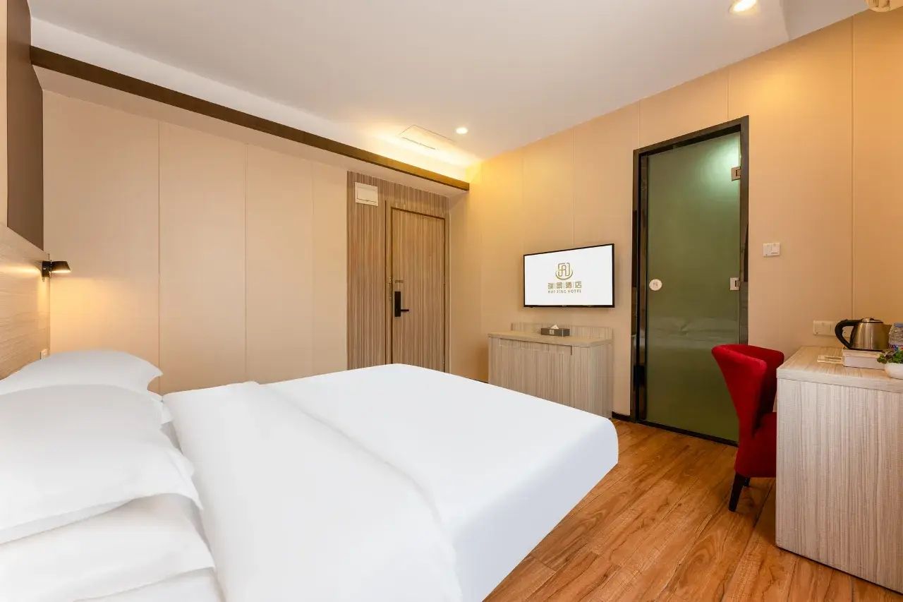 A hotel room with a bed, a desk, a chair, a television, and a door.