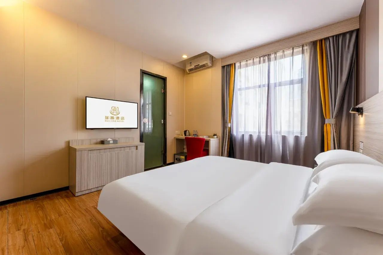 Habitación de hotel con cama, escritorio, silla, televisión y ventana con cortinas.