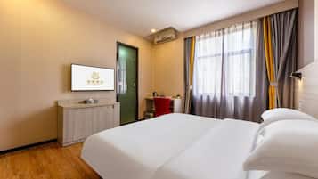 Habitación de hotel con cama, escritorio, silla, televisión y ventana con cortinas.