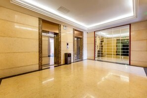 A hotel lobby with a polished marble floor, elevators, and a glass partition wall.